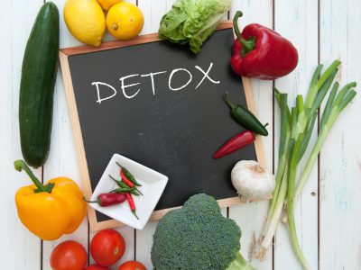 Detox handwritten on a chalkboard surrounded by fresh vegetables